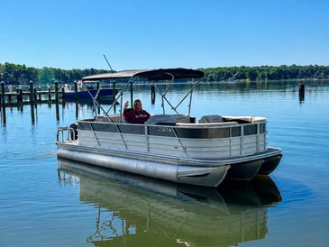Pontoon boat floating calmly on a lake with a person aboard.