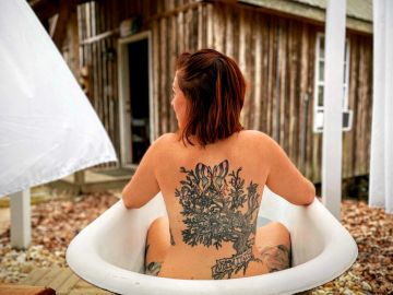 Woman with a large floral tattoo sitting in a vintage bathtub outdoors.