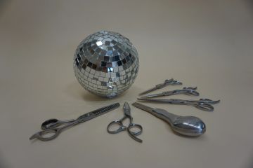 A disco ball surrounded by hairdressing scissors and tools on a beige surface.
