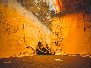 Two people sitting surrounded by walls covered in torn paper sheets.