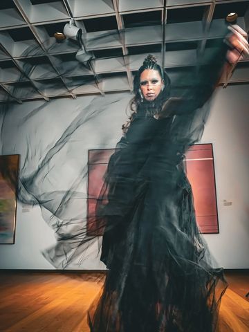 A woman in a flowing black dress striking a dramatic pose indoors.