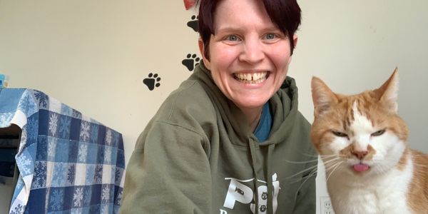 Kat, the owner of Kat and Dogs Ohio, sitting on the ground with a cat who is sticking out his tongue