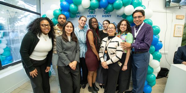 A group of diverse professionals posing under a blue and white balloon arch.