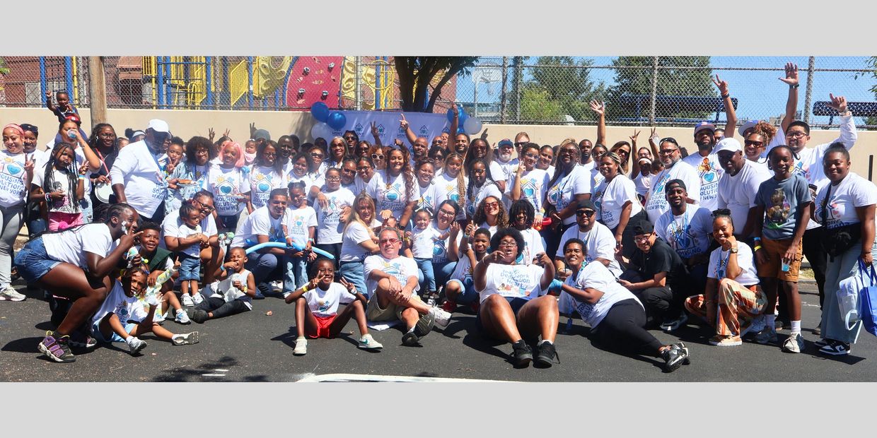 Large group of diverse people in matching shirts posing outdoors at a community event.
