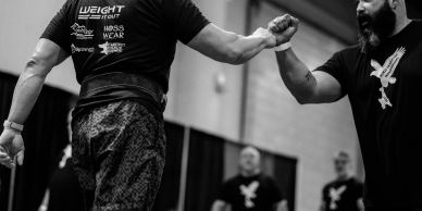 Two men fist bump indoors.