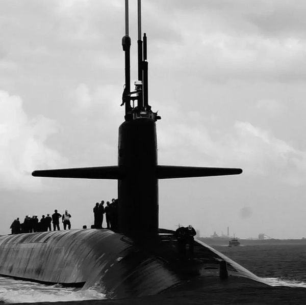 Silhouette of a submarine with crew on deck against a cloudy sky.