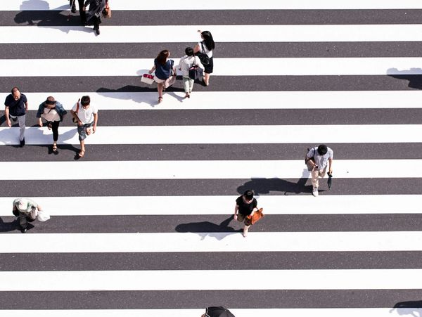 People crossing a wide zebra-striped pedestrian crosswalk on a sunny day.