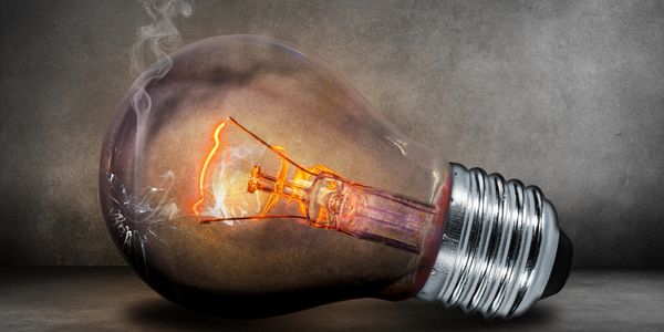 A broken, smoking light bulb with a glowing filament on a dark surface.