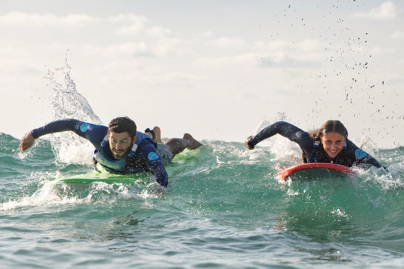 Two surfers paddling on surfboards through the ocean waves.