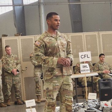 A soldier in uniform speaks in front of a group inside a military facility.