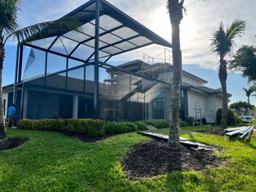 House with new screened enclosure under construction in sunny yard.