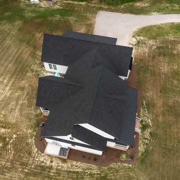 Aerial view of a house with a black roof and surrounding yard.