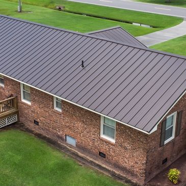 A brick house with a sleek metal roof and a wooden deck.