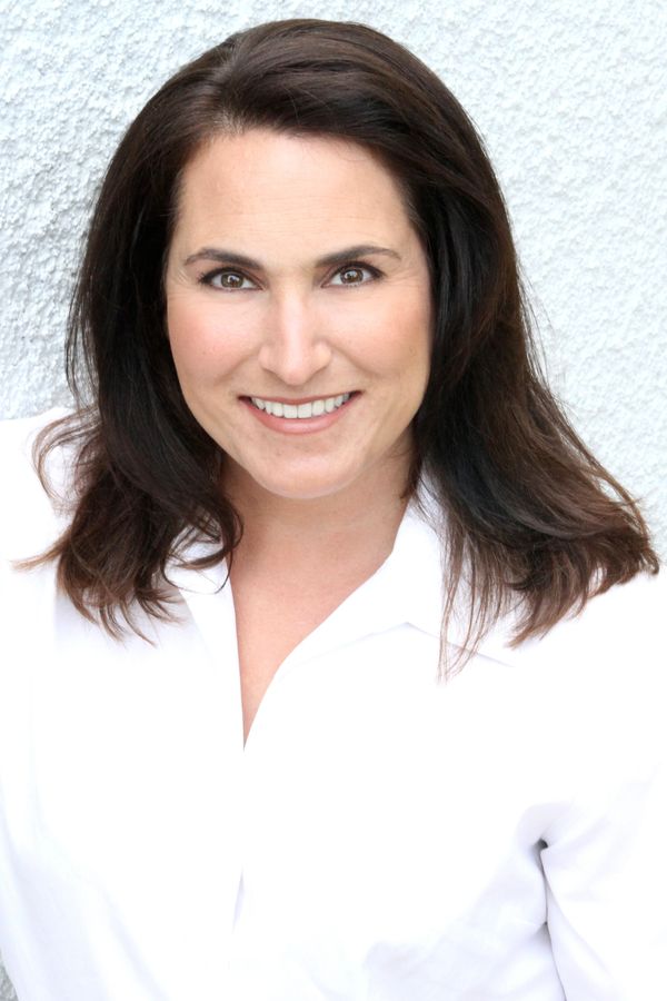 Smiling woman with dark hair in a white shirt against a textured light background.