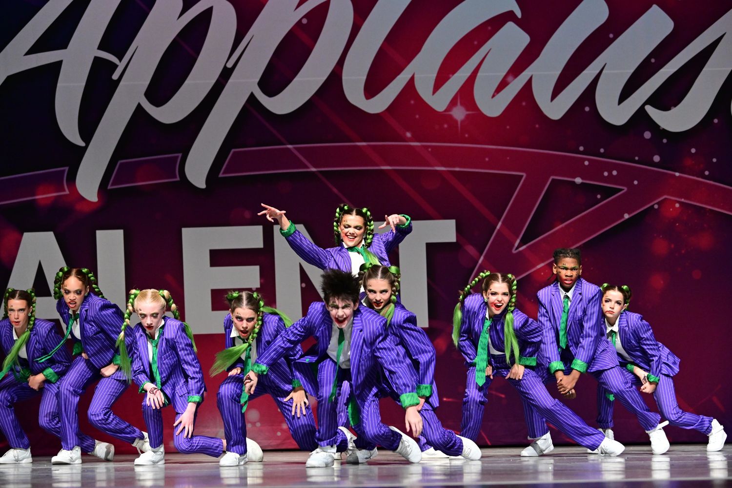 Youth dance group in vibrant purple suits with green accents performing on stage.