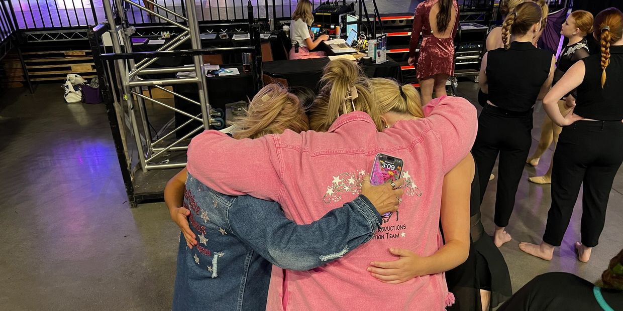 Three people embrace in a group hug backstage at an event.