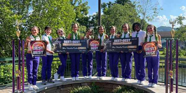 Youth dance team holding trophies and awards outdoors.