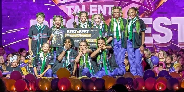 Winning dance team celebrates on stage with trophy and banner.