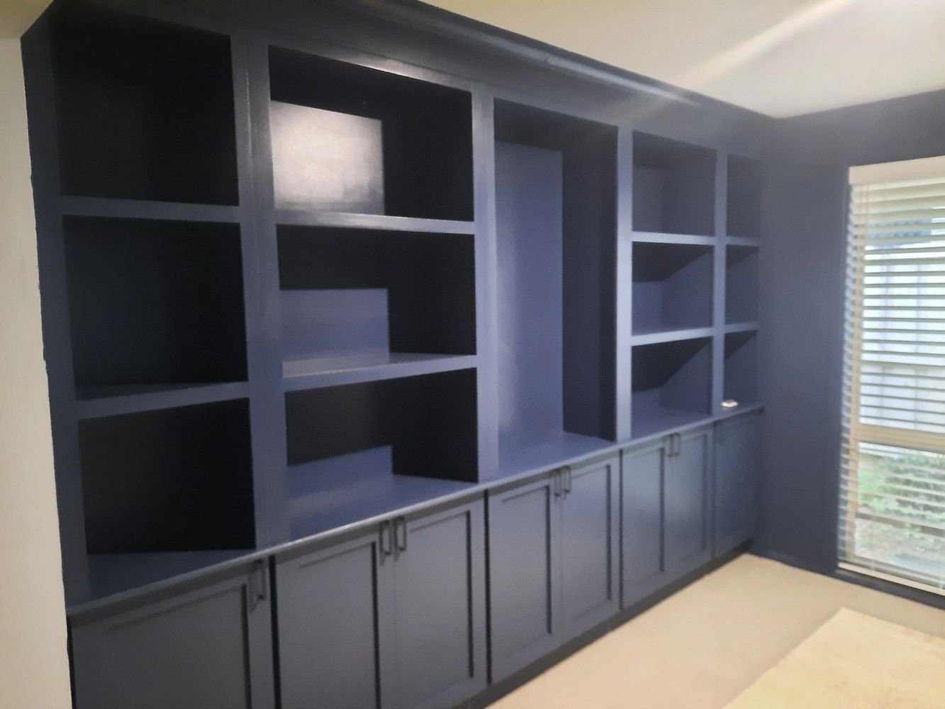 Large navy blue built-in bookshelf with multiple open shelves and closed cabinets.
