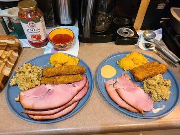 Two plates filled with ham, mashed potatoes, and other food