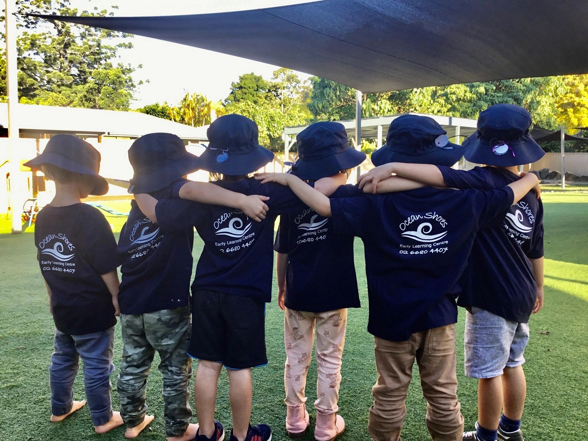 Six children in matching shirts and hats with arms around each other.