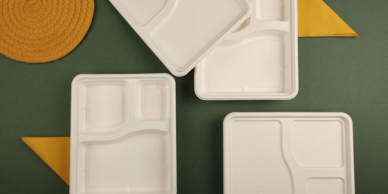 Empty white compartmentalized trays on a green surface with yellow napkins.