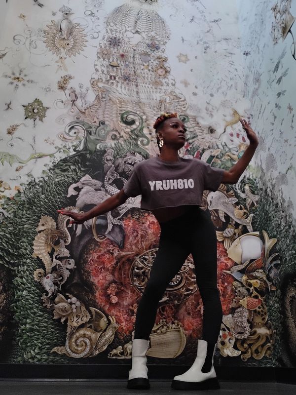 Person posing in front of a detailed, artistic wall mural.