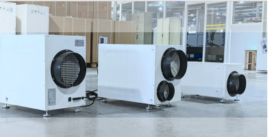 Three white industrial air purifiers arranged in a factory setting.