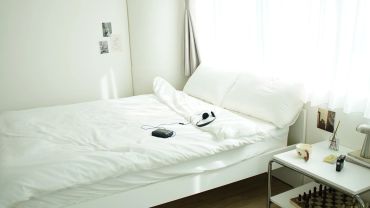 Cozy white bedroom with a neatly made bed and soft natural light.