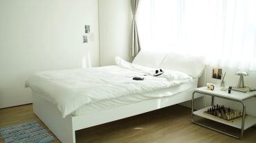 Minimalist bedroom with white bed and natural light from window.