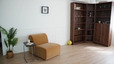 A minimalist living room with a brown chair, side table, and wooden shelves.