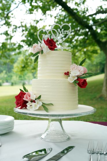 Two-tier white wedding cake with red and pink flowers.