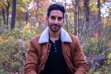 Man in brown jacket sitting outdoors in autumn.