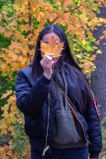 Person holding a fall leaf covering their face.