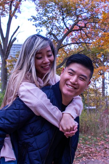 Couple enjoying a piggyback ride in autumn park with colorful foliage.