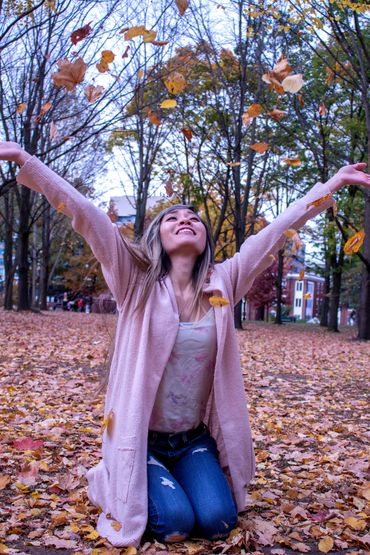 Woman joyfully throwing autumn leaves outdoors.