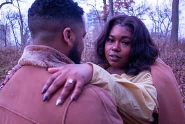 Couple embracing outdoors with woman showing an engagement ring.