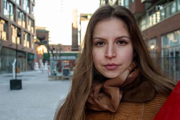 Young woman in brown scarf and jacket in urban setting.