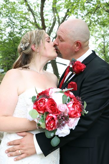 Wedding couple sharing a kiss with bouquet of red and pink flowers.