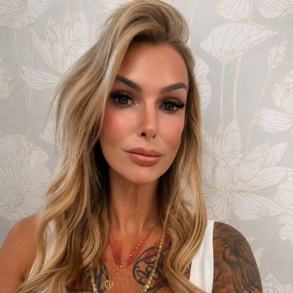 Blonde woman with tattoos and wavy hair posing indoors.