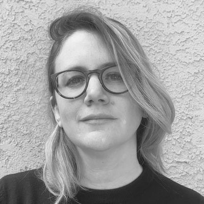 Woman with glasses and blonde hair against a textured wall.