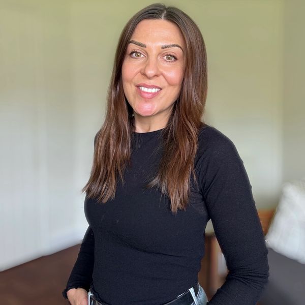 Smiling woman with long brown hair wearing a black top indoors.