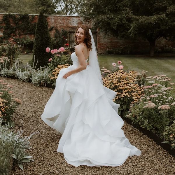 Bride in a flowing white gown smiles in a garden.