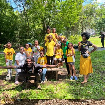 Group of smiling children and adults outdoors holding drawings, wearing colorful clothes.
