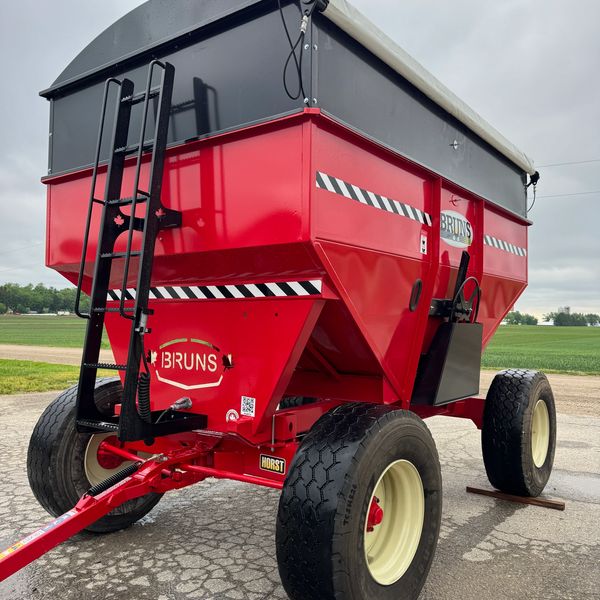 A large red agricultural grain cart with big tires and a ladder on the front.