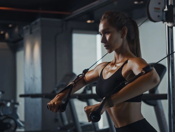 Sporty woman exercising on multistation at gym for arm and shoulders muscles