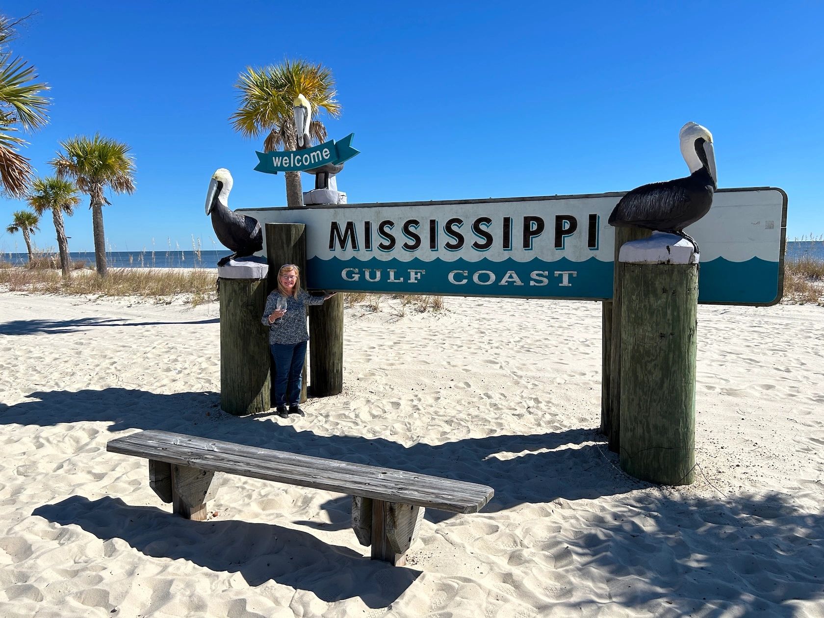 Charlene Jenner in front of the "Welcome to the Mississippi Gulf Coast" sign on the beach in Gulfpor