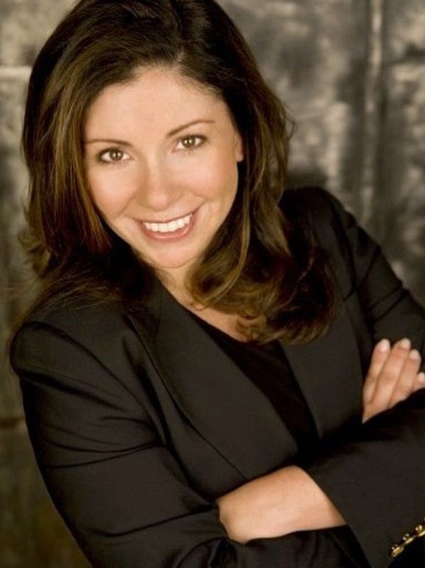 Smiling woman in a black blazer with arms crossed.