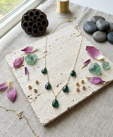 Elegant necklace with green teardrop stones displayed with petals and beads.