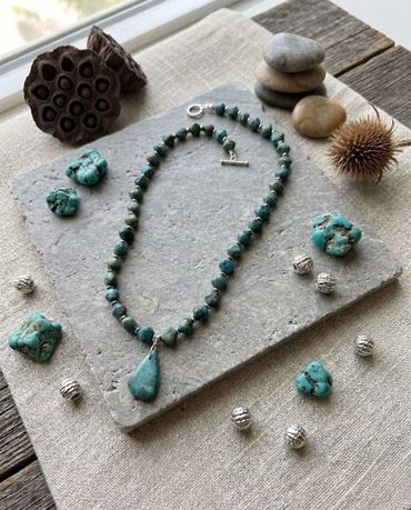 Turquoise beaded necklace with natural stones and silver accents on a stone slab.